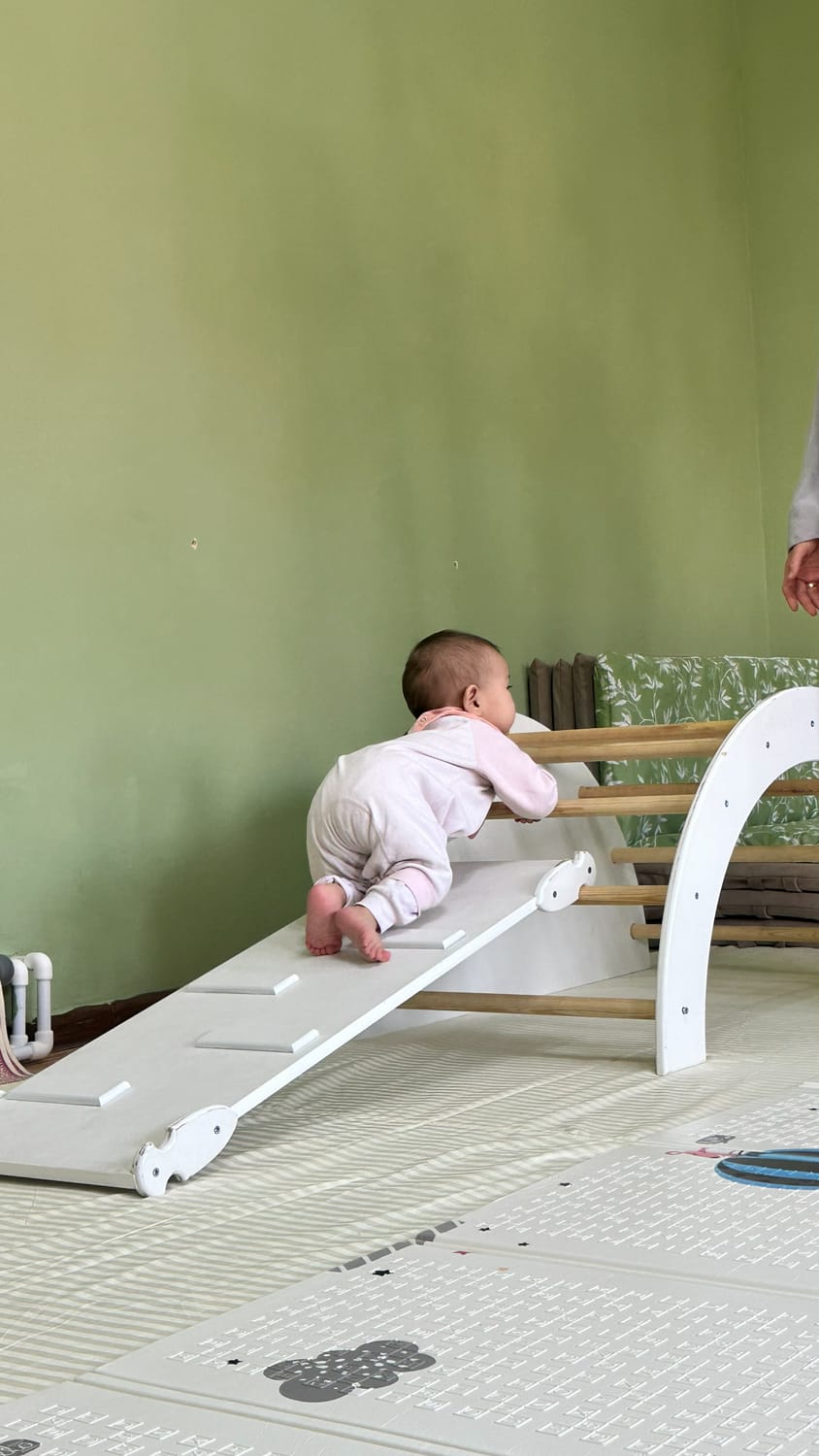 Harakat maydonchasidagi Pikler qiyaligiga chiqayotgan chaqaloq